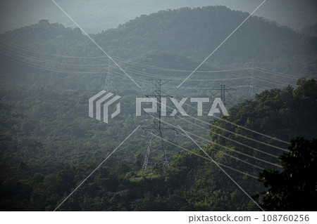 Mist flows through a valley and There are lines of electrical transmission towers high on the mountain. 108760256