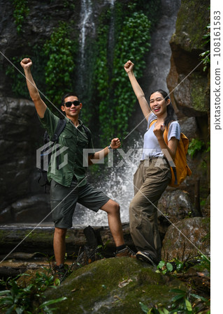 Happy young woman tourist with backpack enjoying tropical waterfall view. Travel and active life concept 108161583