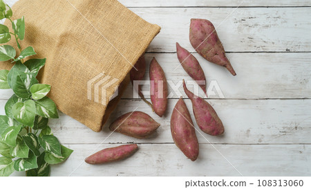 Sweet potato spilling out of a jute bag, white wood grain background 108313060