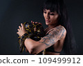 Photo of brunette woman holding yellow anaconda in shadows 109499912