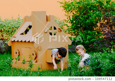 Children are playing in cardboard kid house. Child having fun outdoors. 109547112