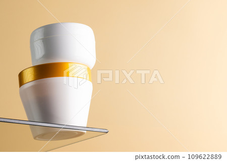 Beauty product white tubs on glass shelf, copy space on orange background 109622889