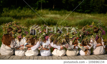 Girls in woven wreaths of different flowers and grass on a warm summer day. 109896134