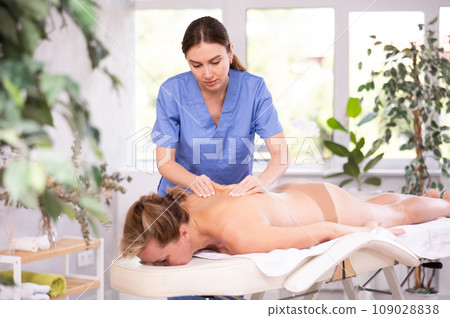 Skilled young masseuse doing back massage to female client 109028838