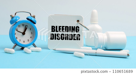 On a blue surface lie pills, an alarm clock and a notebook with the inscription - Bleeding Disorder 110651689