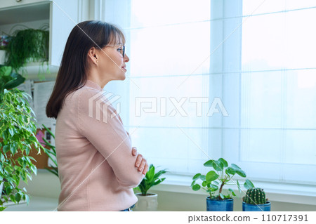 Dreamy, thoughtful middle-aged woman looking out the window at home 110717391