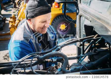 Mechanic repairs engine of tractor or heavy equipment. Farmer inspects and diagnoses agricultural 110814578