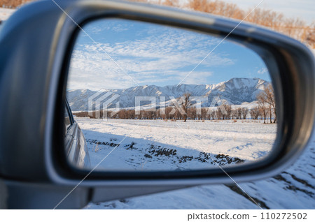 beautiful winter landscape with Tien Shan mountains and trees in field in snow in rearview mirror of car. Concept of festive holiday winter travel in Kazakhstan 110272502