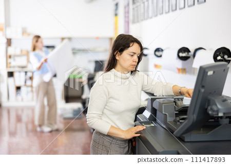 Woman using printer while working in print shop 111417893