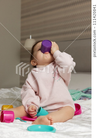 happy cute little child girl playing and pretending drinking tea from toy cups on bed 111420841