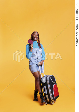 Joyful traveller with passport leaving on international getaway, feeling excited about holiday destination. Female model travelling on vacation trip with identification pass, trolley bags. 111486393