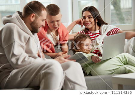 Father and son discussing something looking in tablet and little girl sitting with laptop and mother listening husband and boy. 111514356