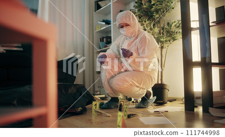 A crime investigator in a protective suit is working with marked evidence on the floor 111744998