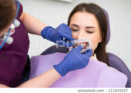 Orthodontist inserts an elastic ring into the mouth of the patient 111839107