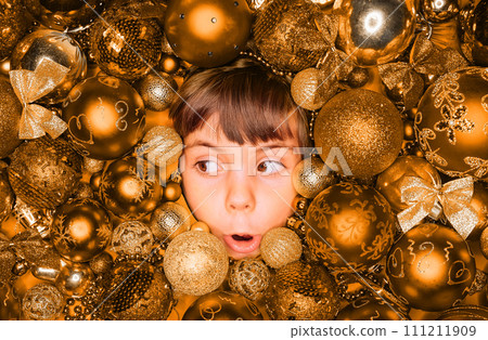 Surprised little boy face with joy in golden Christmas tree toys balls. Holiday. 111211909