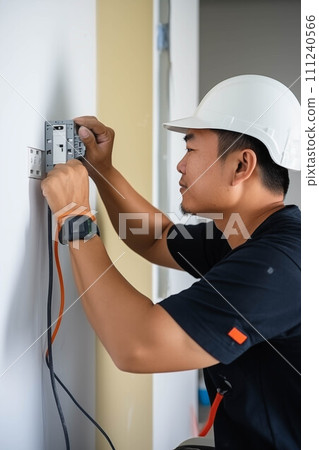 Asian male electrician installing electrical outlets. 111240566