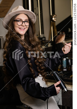 Female portrait of a hairdresser. A young barber girl blows her hair with air from the dryer. 112538456