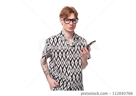 a young european guy with red hair wears glasses for vision correction and holds a phone in his hand 112693766