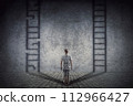 Person stands in front of a wall casting two ladder shadows with one broken on the left and another ready to use on the right. Dilemma and choice concept between good and bad 112966427