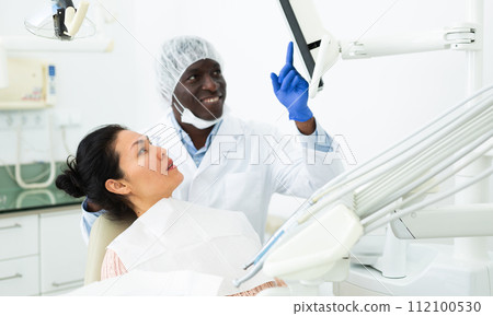 Positive dentist discussing teeth x-ray and treatment procedures with female patient 112100530