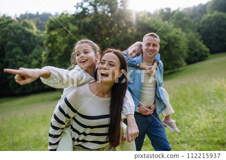 Portrait of beautiful family, parents piggibacking two daughters, having fun in nature. 112215937