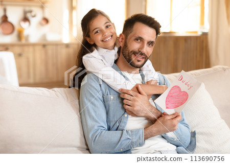 Girl hugs father holding a handmade card 113690756