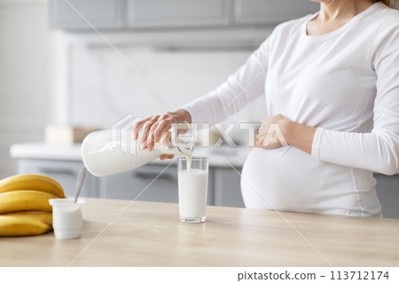 Pregnant woman in kitchen pouring milk in kitchen 113712174