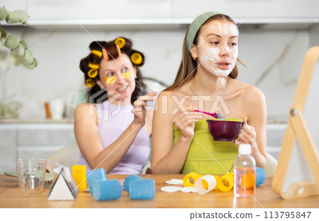 Woman applying facial mask during home spa day with bestie 113795847