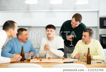 Group of friends excitedly playing board games and drinking beer at home 113232348