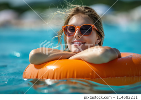 A Caucasian woman in orange sunglasses relaxes on an orange float in a pool, enjoying summer 114682211