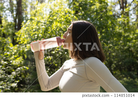 young woman drinks water from a bottle during exercise 114851014