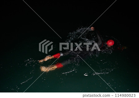 A determined professional triathlete undergoes rigorous night time training in cold waters, showcasing dedication and resilience in preparation for an upcoming triathlon swim competition 114980023