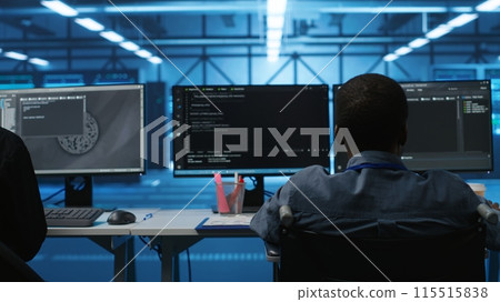 Person with disability next to multiracial coworkers in data center coding on computer. Wheelchair user and multiethnic team working together, doing programming, overseeing server clusters 115515838