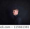 Thoughtful young man side view portrait, looks upset and tired against a dark wall background. Stressed male student feels emotional discomfort and anxiety problems 115661381