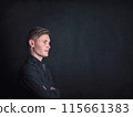 Positive thinking young man side view portrait, looks confident holding arms crossed against a black wall background. Male student reflecting with optimism 115661383