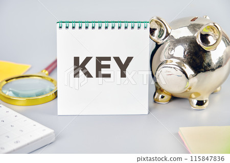 KEY word on a blank sheet in a notebook in a composition with a piggy bank, magnifying glass, calculator, stickers on a gray background 115847836