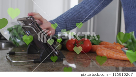 Image of hearts over caucasian man cooking and using tablet 115910267