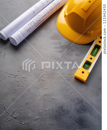 Yellow hard hat, blueprints, and a spirit level on a concrete surface, tools of the trade for builders 115942450