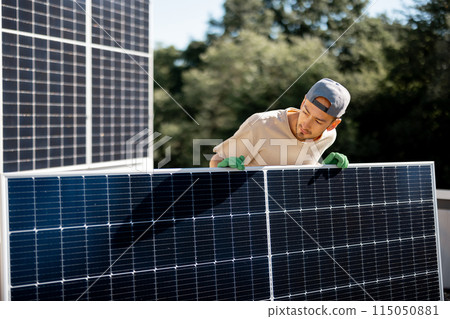 Man installing solar panels on a roof of his house 115050881