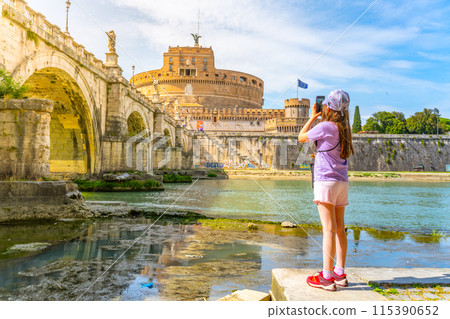 A young girl captures a photo of Castel SantAngelo and a bridge in Rome with her smartphone on a bright sunny day. Rome, Italy 115390652