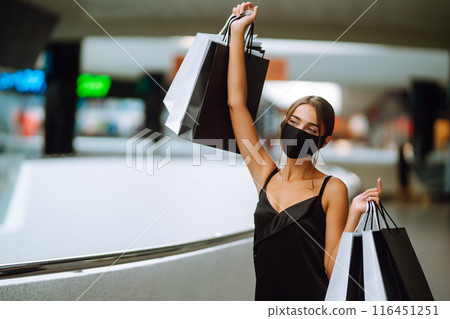 Young woman in protective black medical mask on her face with shopping bags in the mall.Covid-2019. 116451251