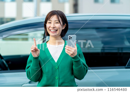 Smiling woman holding a smartphone in front of a car Smartphone and car 116546480