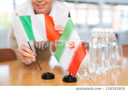 Little flag of Iran on table and flag of Italy put next to it by young woman 116583959