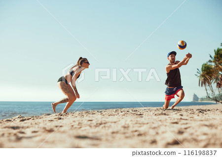 Dynamic image of competitive and joyful young people, men and women in sportswear playing beach volleyball in the morning. 116198837