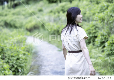 A woman strolling through a park with fresh greenery 116283053