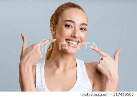 Orthodontic concept. Happy girl showing her beaming white teeth with two forefingers, grey background 117499502