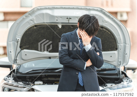 Young Asian man shocked in front of a car (road service, trouble, rescue, trouble) 117557592