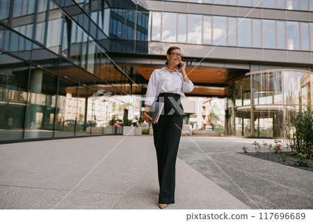 A Confident Businesswoman is Walking Gracefully in an Urban Environment with Purpose and Focus 117696689