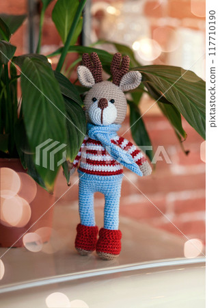 Christmas deer. Closed up toy amigurumi deer in striped sweater and stylish blue scarf. 117710190