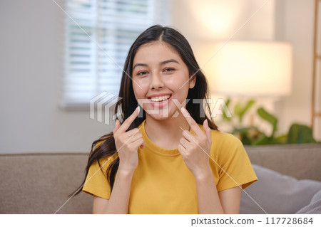 A woman in a yellow shirt is smiling and showing her teeth 117728684